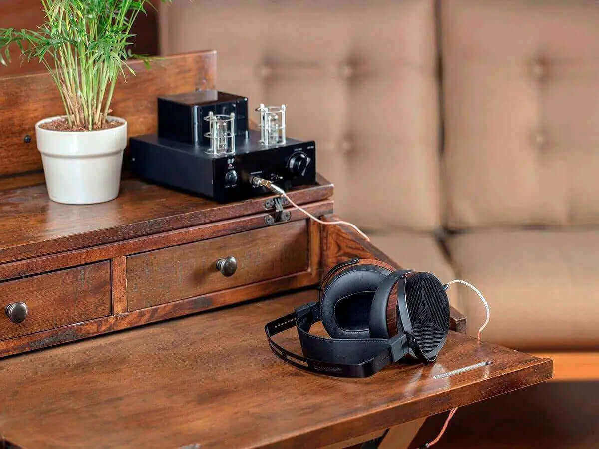 Monolith M1060 headphones placed next to a stylish audio amplifier on a wooden desk, showcasing a sleek home setup.