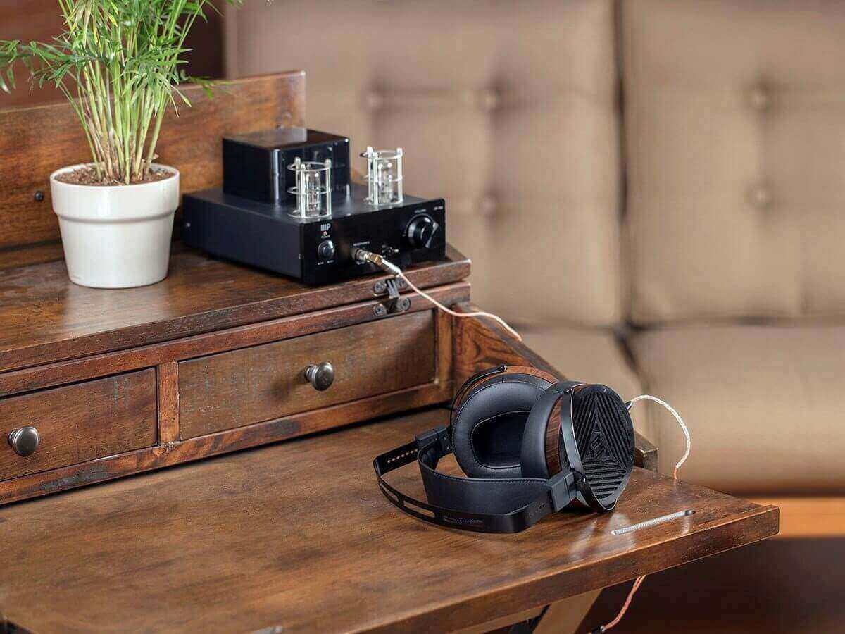 Monolith M1060 planar headphones on a wooden desk with a vintage amp, perfect for audiophile listening.